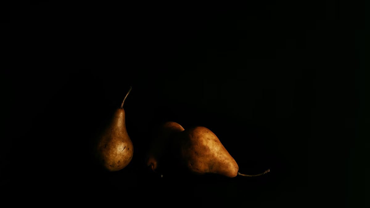 Dramatic still life of ripe pears in low lighting against a black background.
